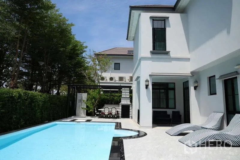 Detached House for rent or sale in Saphan Sung, Bangkok - Private swimming pool with sun loungers and patio beside white house.