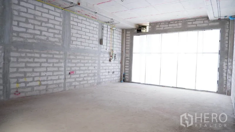 Retail Space for rent in Khlong Toei, Bangkok - Unfinished retail shell with large frosted glass frontage, concrete floor, and exposed ceiling conduits.