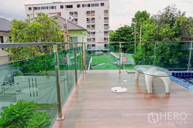 独立式住宅 出售在Lat Phrao, Bangkok - 泳池平台木纹地面与玻璃栏杆，俯瞰社区景观。