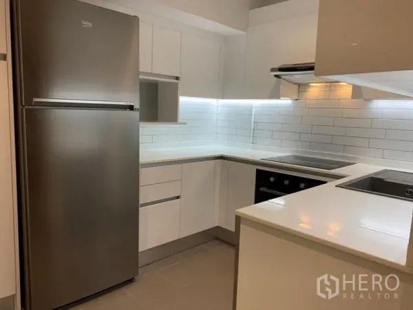 Condominium for sale in Watthana, Bangkok - Modern U-shaped white kitchen with stainless refrigerator, oven and subway tile backsplash.
