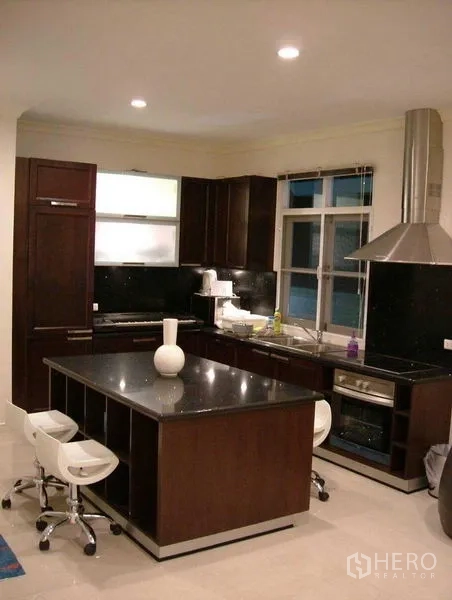 Detached House for rent in Prawet, Bangkok - U-shaped kitchen with dark wood cabinetry, stone island and stainless range hood.