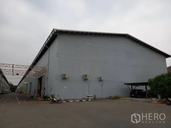 Warehouse for rent in Mueang Pathum Thani, Pathum Thani - Warehouse exterior with wall-mounted air-conditioning units and a sheltered parking bay.