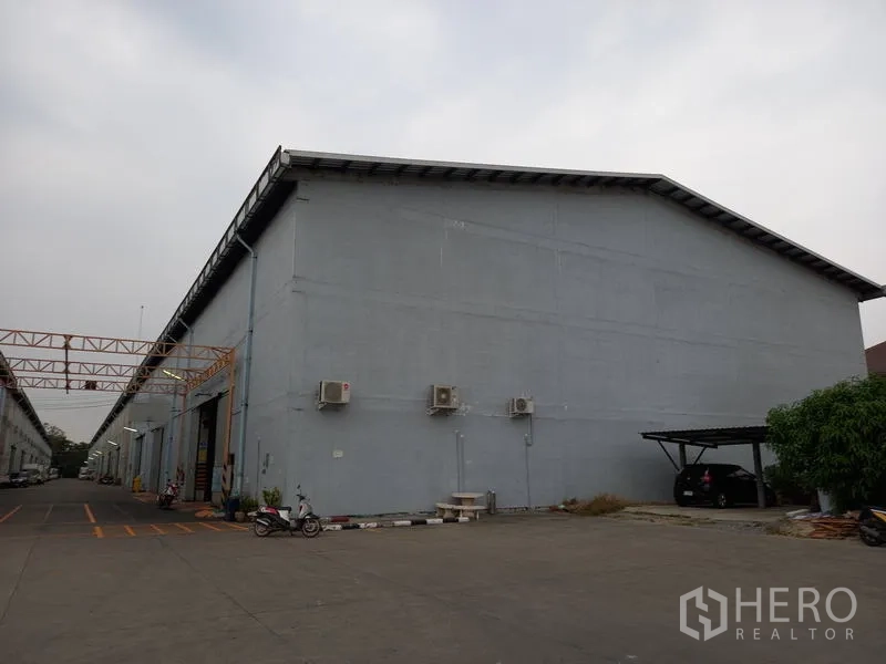 Warehouse for rent in Mueang Pathum Thani, Pathum Thani - Warehouse exterior with wall-mounted air-conditioning units and a sheltered parking bay.