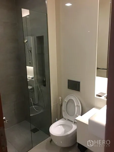 Condominium for rent or sale in Khlong Toei, Bangkok - Modern bathroom with glass-enclosed shower, toilet and sleek vanity lighting.
