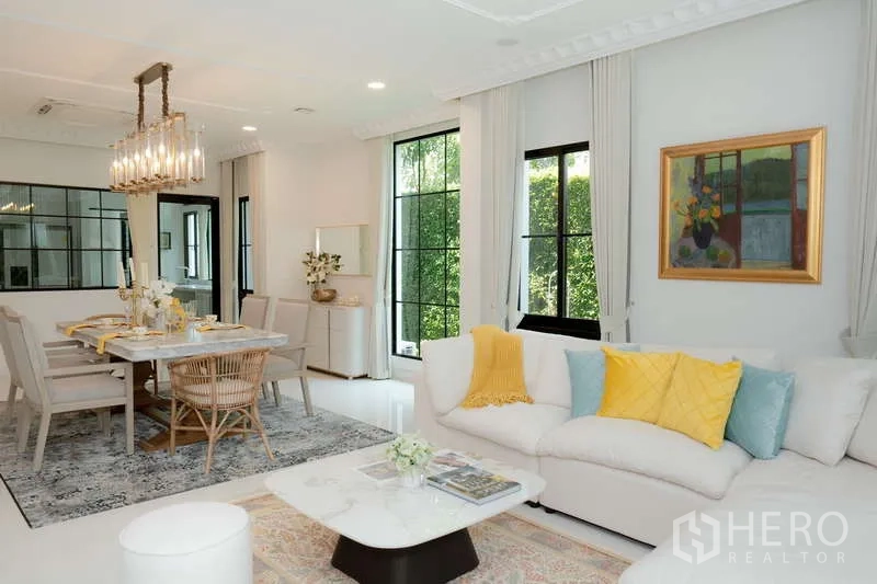 Detached House for rent or sale in Saphan Sung, Bangkok - Open-plan living and dining room with sectional sofa, large windows and statement chandelier.