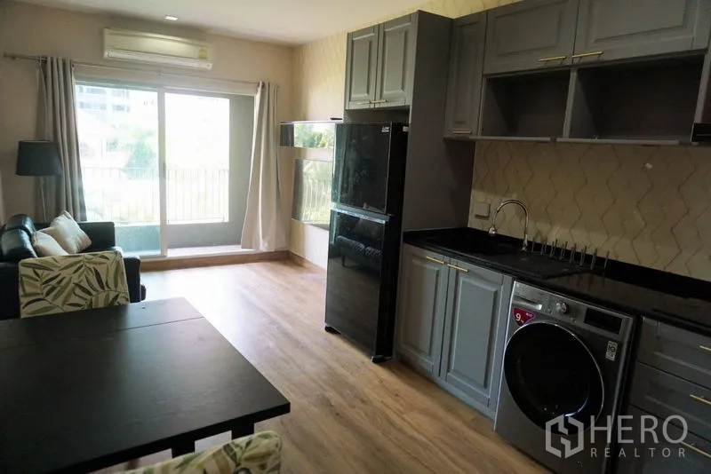Condominium for sale in Khlong Toei, Bangkok - Bright living area with sliding doors to the balcony and a full grey kitchen along one wall.