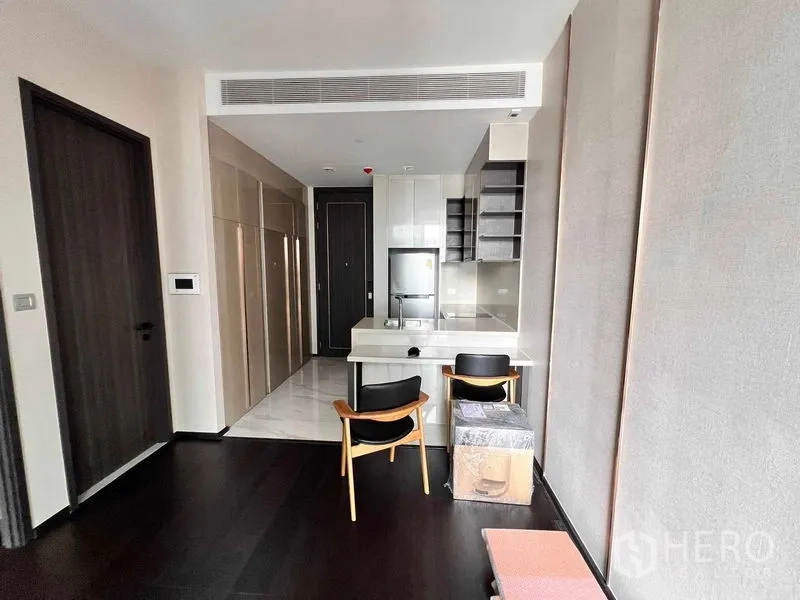 Condominium for rent in Watthana, Bangkok - Open-plan lounge with kitchenette, storage wall, and dining chairs.