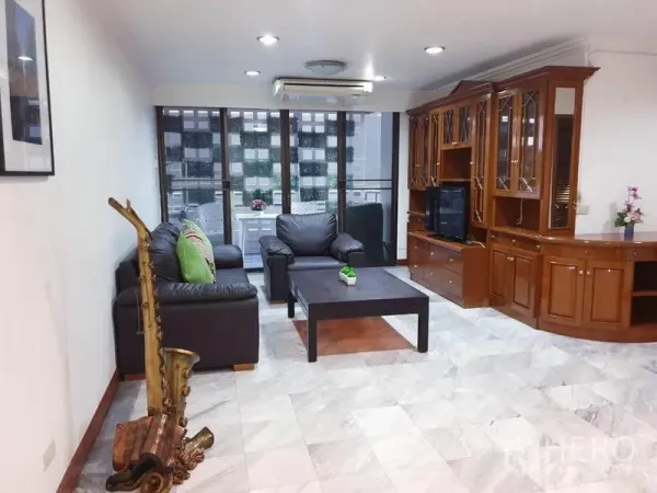 Condominium for rent or sale in Watthana, Bangkok - Bright living room with leather sofas, marble floor and built-in wooden cabinet facing balcony windows.