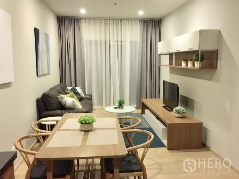 Condominium for rent in Bangkok - Open-plan living and dining area with wooden table, TV console, sofa and floor-to-ceiling curtains in a modern Bangkok condo.