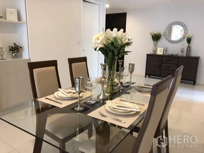 公寓 出租在Watthana, Bangkok - 优雅的餐桌摆设，鲜花与银色餐具，背景有边柜与圆形镜子。