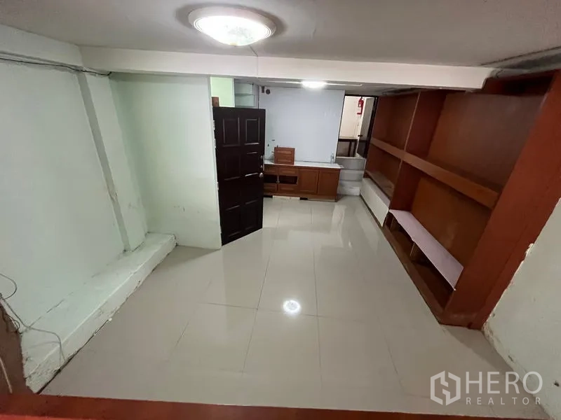 Shophouse for rent in Khlong Toei, Bangkok - Room with glossy tiled floor, wood shelves, and a dark wooden door.