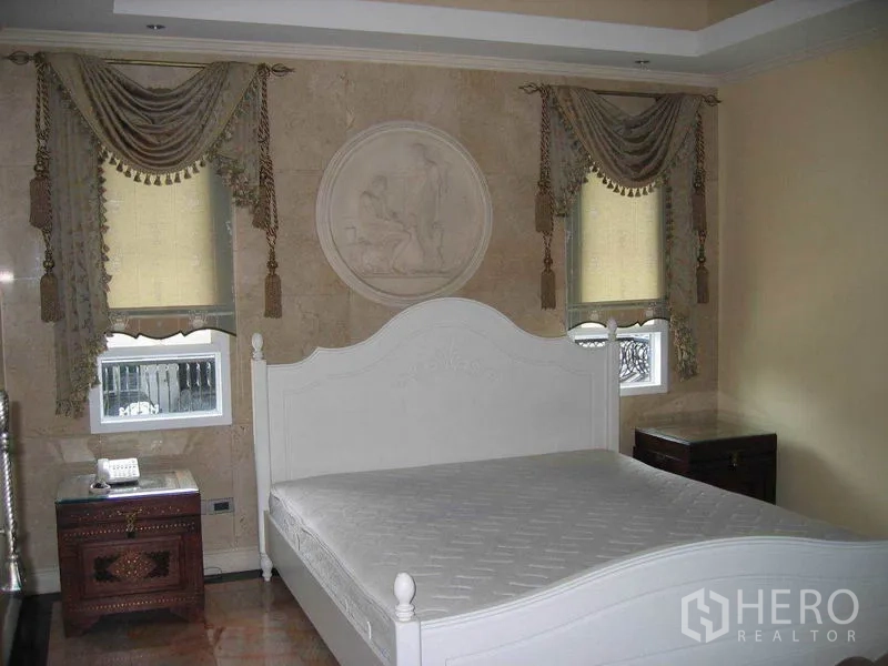 Detached House for rent in Watthana, Bangkok - Bedroom featuring a white bed, carved wall medallion and elegant curtains.