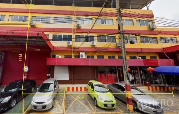 货栈 出租在Bang Phli, Samut Prakan - 红黄相间的商业建筑外立面，前方有划线停车位与卷帘门，标注有门面尺寸。