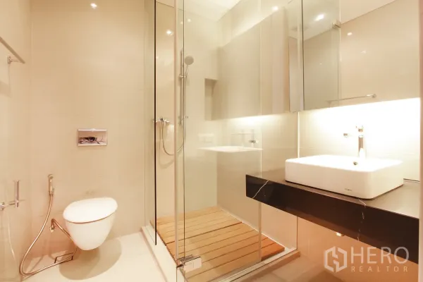 Condominium for sale in Bang Rak, Bangkok - Modern bathroom with glass-enclosed shower, wall-mounted toilet and illuminated vanity.