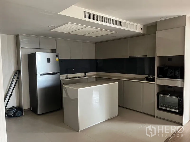 公寓 出租在Pathum Wan, Bangkok - U形现代厨房，亮面橱柜，中岛，烤箱、微波炉和不锈钢冰箱齐全。