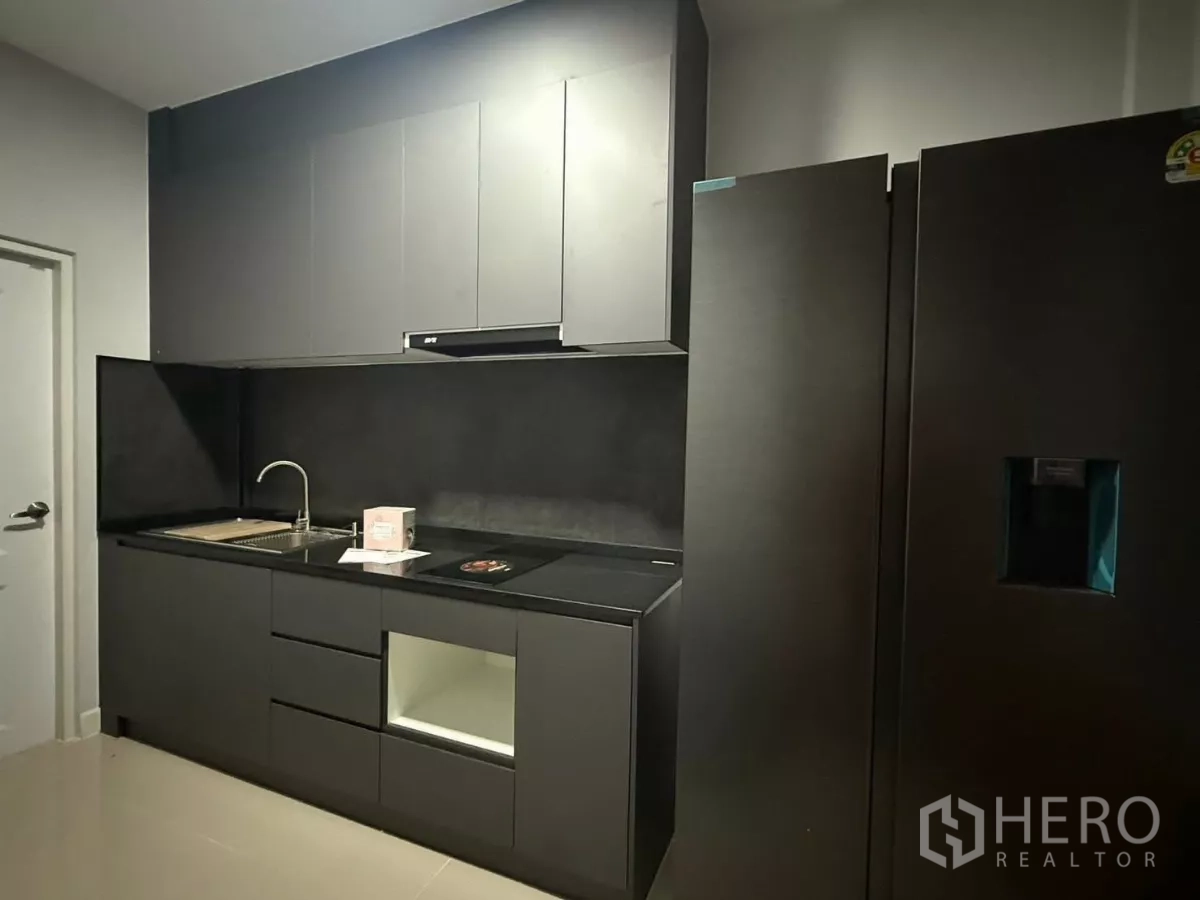 Detached House for rent in Bang Phli, Samut Prakan - Modern dark-tone kitchen with built-in cabinets, sink and cooktop.