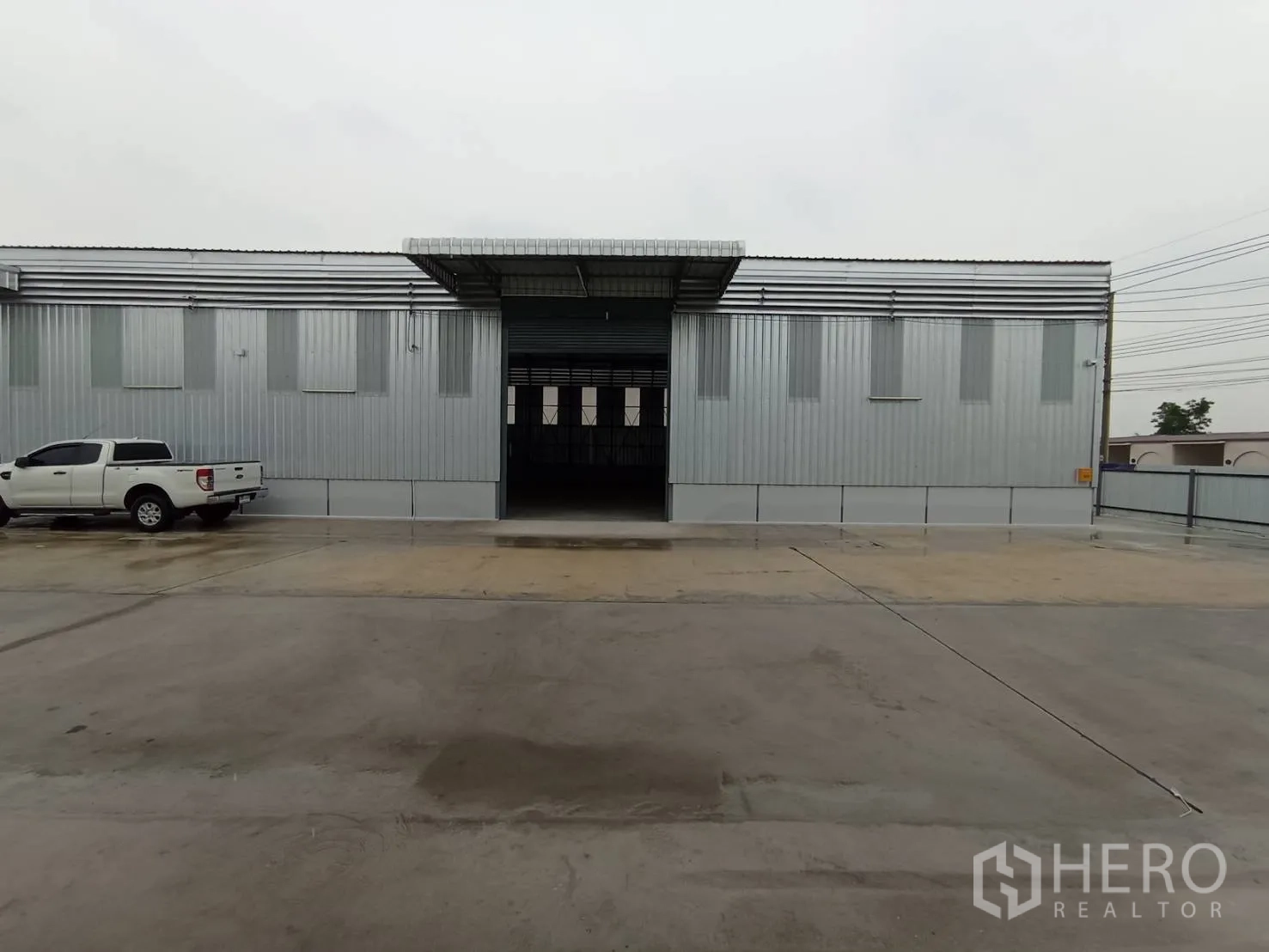 Warehouse for rent in Mueang Samut Prakan, Samut Prakan - Metal-clad warehouse exterior with a wide roller shutter and large concrete driveway.