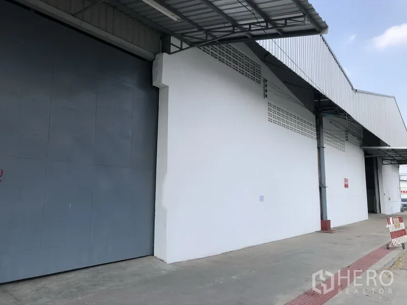 คลังสินค้า ให้เช่าในNonthaburi - ภายนอกอาคารโกดัง ประตูสไลด์เหล็กสีเทาขนาดใหญ่ และชานโหลดมีหลังคาริมทางวิ่งกว้าง
