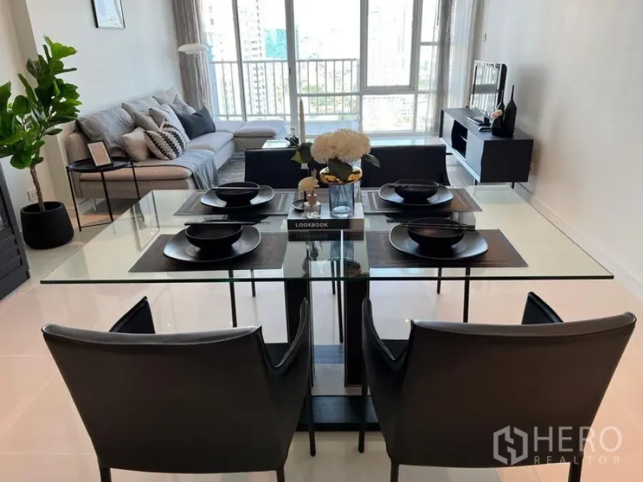 Condominium for rent in Watthana, Bangkok - Open-plan living and dining area with a glass-top table, sofa, and floor-to-ceiling windows offering Bangkok city views.