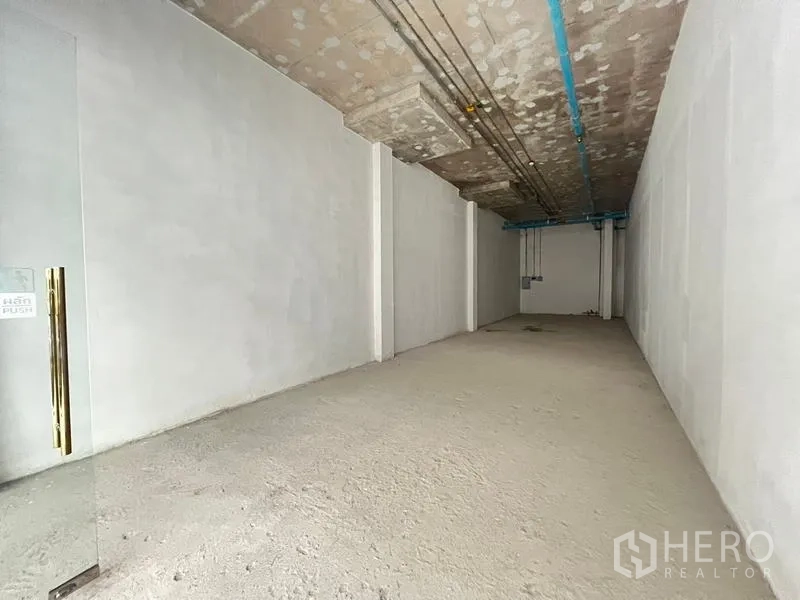 Retail Space for rent in Khlong Toei, Bangkok - Long, narrow interior with high ceiling, exposed pipes, and white plaster walls.