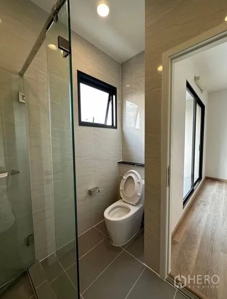 Townhouse for rent in Yan Nawa, Bangkok - Compact bathroom with glass shower, window and modern toilet.