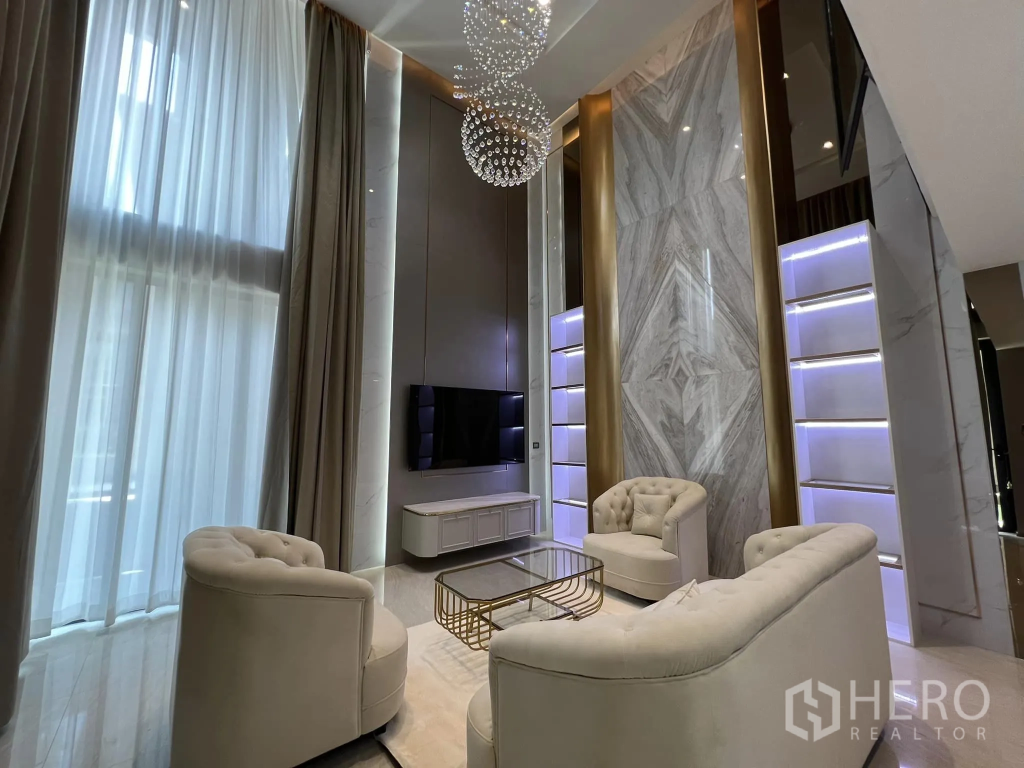 Detached House for rent or sale in Yan Nawa, Bangkok - Double-height living room with tufted sofas, TV and a marble feature wall.