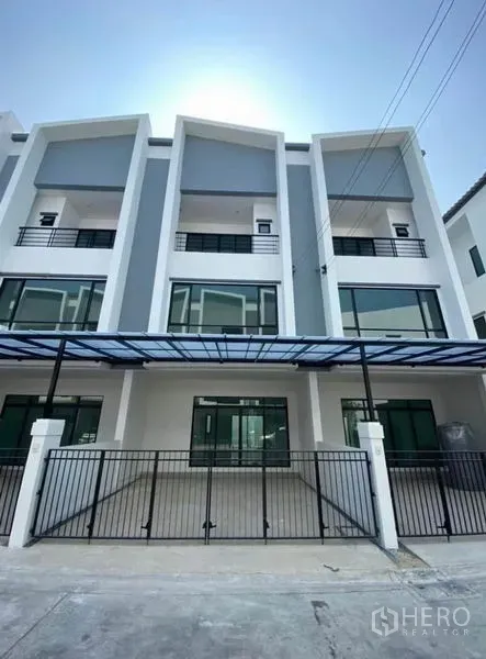 Townhouse for rent in Bang Na, Bangkok - Modern three-storey townhouse facade with gated parking and glass-front balconies.