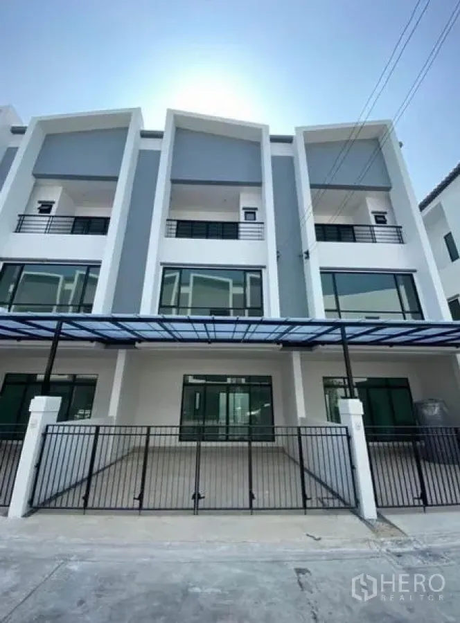 Townhouse for rent in Bang Na, Bangkok - Modern three-storey townhouse facade with gated parking and glass-front balconies.