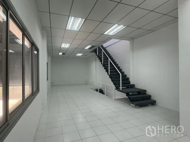 Factory for rent in Khlong Luang, Pathum Thani - Long office area with staircase and sliding windows overlooking the factory floor.