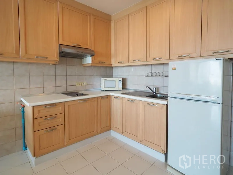 Condominium for rent in Sathon, Bangkok - L-shaped kitchen with light wood cabinets, cooktop, hood, microwave and refrigerator in a Bangkok condo.