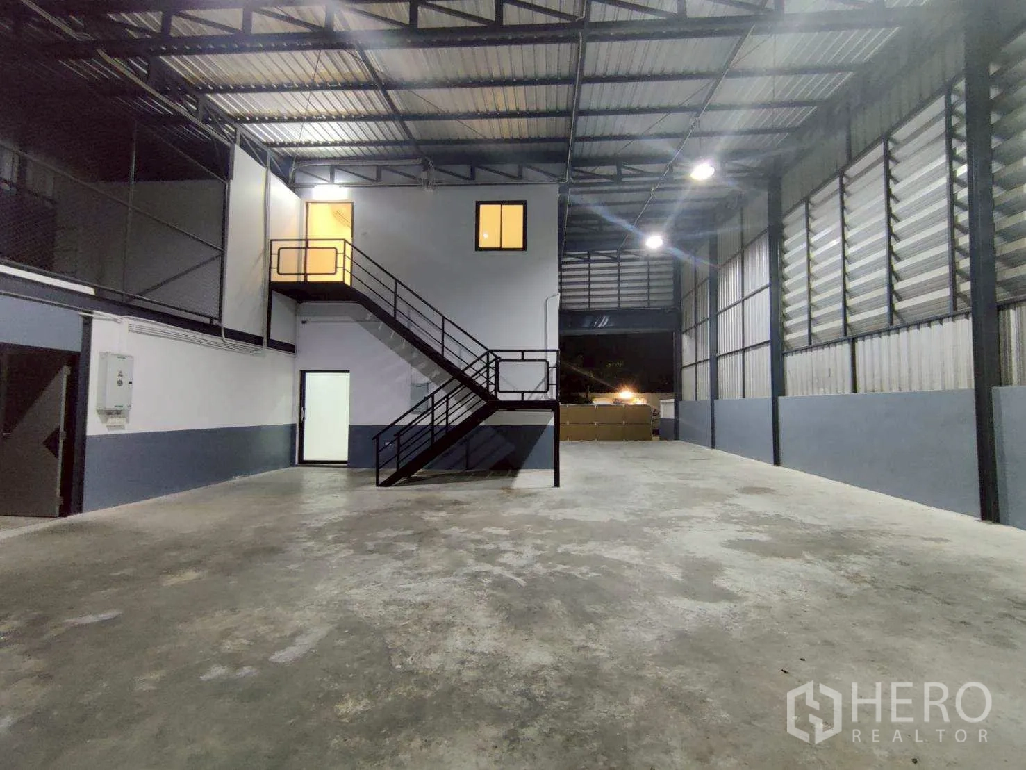 Warehouse for rent in Lam Luk Ka, Pathum Thani - High-ceiling warehouse interior with concrete floor and mezzanine office with stairs.