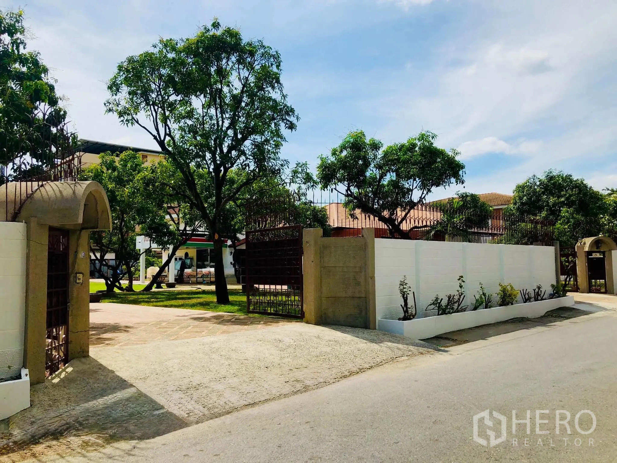 Home Office for rent in Bang Na, Bangkok - Gated entrance with tall trees and a walled perimeter along a quiet street.