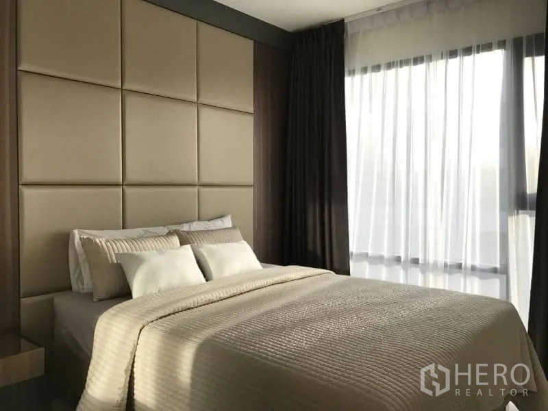 Condominium for rent or sale in Khlong Toei, Bangkok - Bright bedroom with padded headboard and sheer curtains.