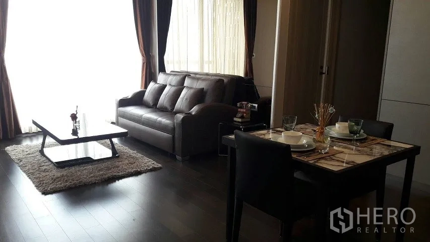 公寓 出租或出售在Watthana, Bangkok - 客厅与餐区一体，皮质沙发、深色木地板、落地窗与大理石餐桌。