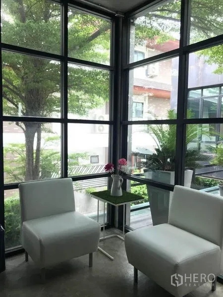 办公空间 出租在Bang Kapi, Bangkok - 休闲角，两把白色单椅，落地窗外是绿色景观。