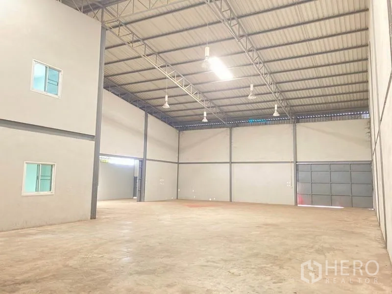 Warehouse for rent in Bang Phli, Samut Prakan - Spacious warehouse hall with high steel-truss ceiling, bright lights and concrete floor.