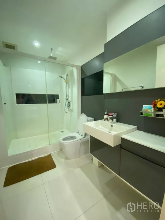 Condominium for rent in Phra Khanong, Bangkok - Modern bathroom with glass-enclosed rain shower, vanity, and toilet.