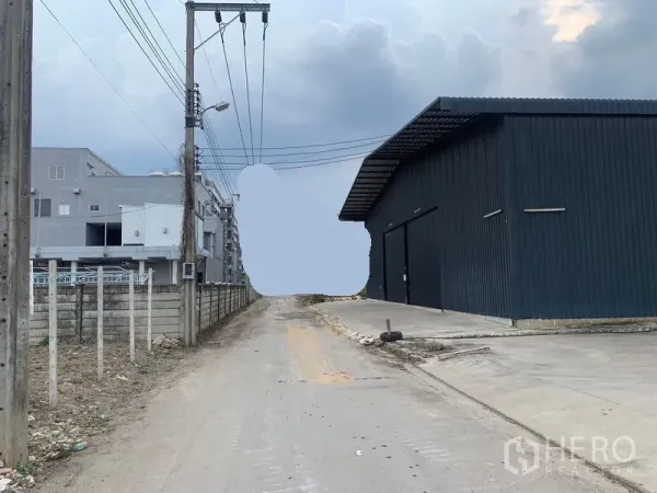 Warehouse for rent in Khan Na Yao, Bangkok - Narrow access road beside the warehouse with power lines and a concrete apron for truck entry.