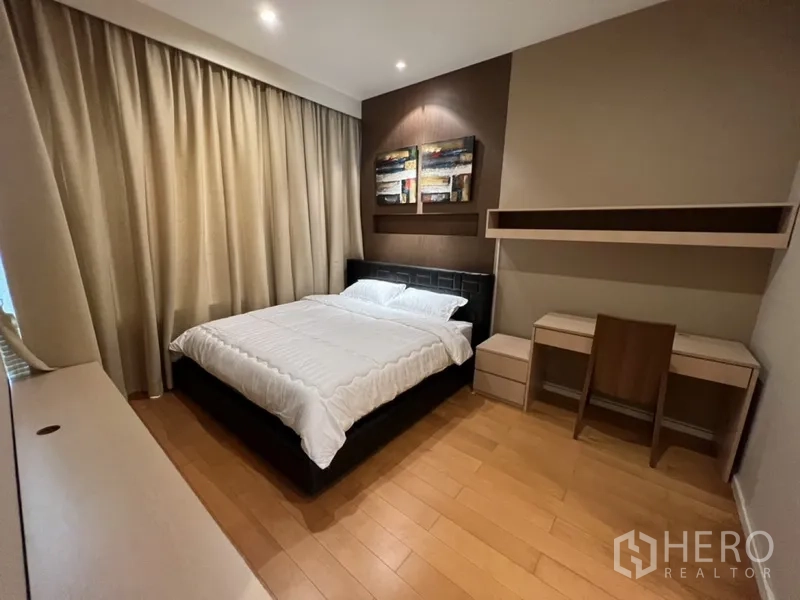 Condominium for rent in Chatuchak, Bangkok - Bedroom with king bed, spotlighted feature wall, desk and shelving, and floor-to-ceiling curtains.