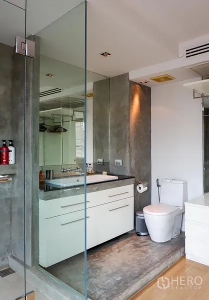 Condominium for rent or sale in Khlong Toei, Bangkok - Modern bathroom with glass shower enclosure, vanity and concrete accents.
