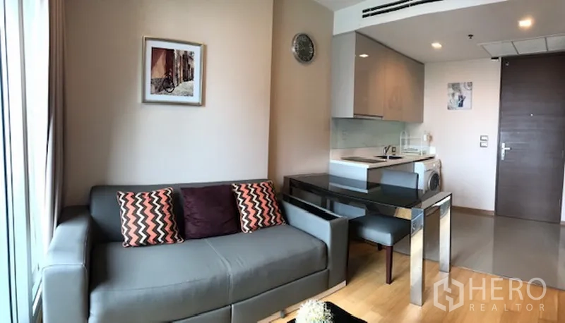 Condominium for rent in Ratchathewi, Bangkok - Open-plan lounge with sofa, dining table and compact kitchen by the entrance.