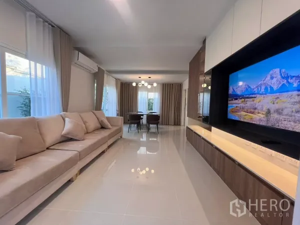 บ้าน ให้เช่าในBang Phli, Samut Prakan - ห้องนั่งเล่นสว่างโทนอบอุ่น โซฟายาว พื้นกระเบื้องเงา และผนังทีวีต่อเนื่องสู่โซนทานข้าว