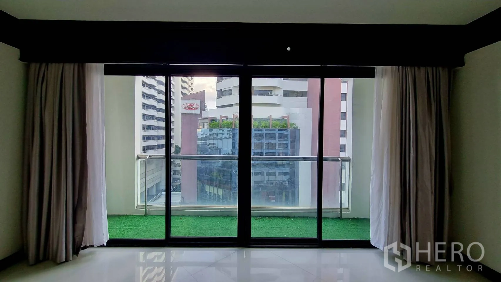 Condominium for rent in Watthana, Bangkok - Balcony with green turf flooring and city view through glass doors.