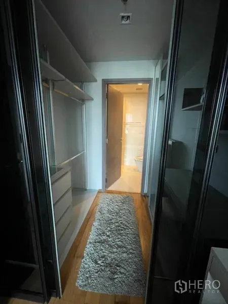 Condominium for rent in Khlong Toei, Bangkok - Walk-in closet corridor with glass wardrobes and rug leading to the bathroom.