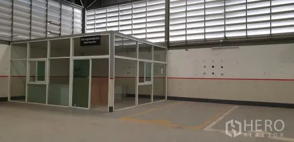 Warehouse for rent in Lam Luk Ka, Pathum Thani - Warehouse interior showing a glass-partition office cabin beneath a high ventilated roof.