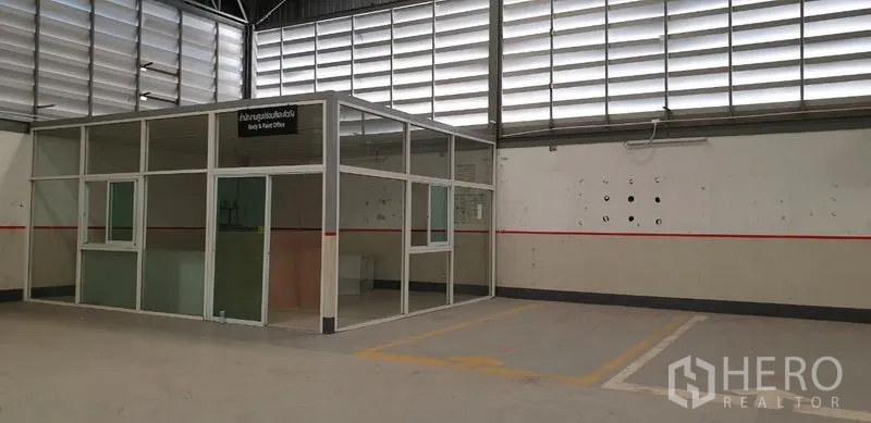 Warehouse for rent in Lam Luk Ka, Pathum Thani - Warehouse interior showing a glass-partition office cabin beneath a high ventilated roof.