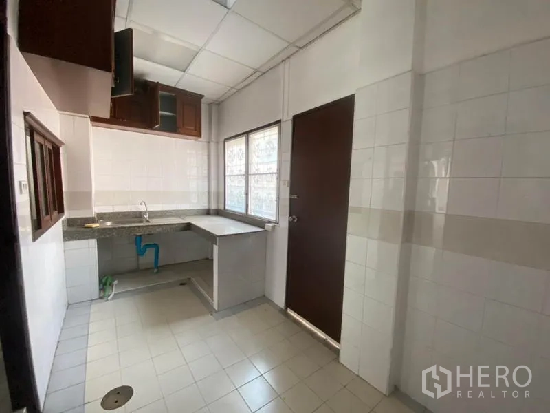 联排别墅 出租在Watthana, Bangkok - 紧凑瓷砖厨房，设台面、水槽、窗户和吊柜。
