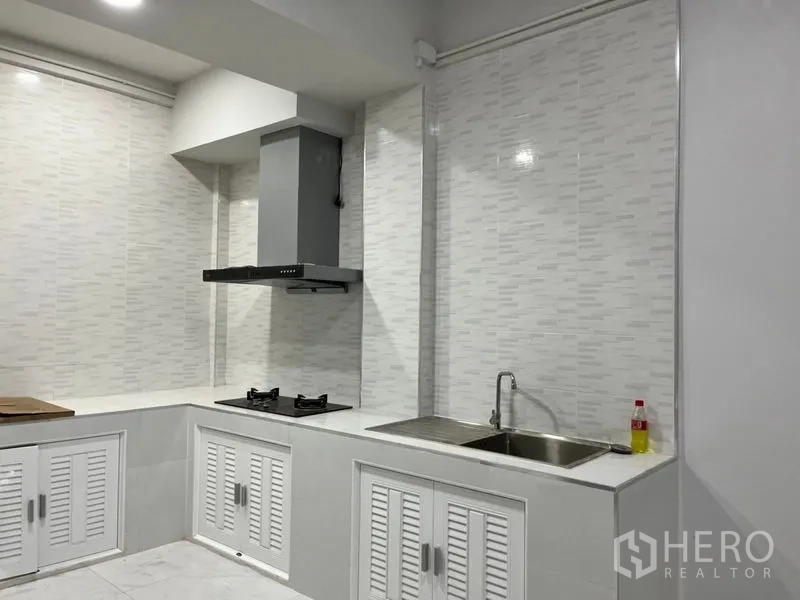 Townhouse for rent in Din Daeng, Bangkok - Modern white kitchen with L-shaped counters, gas hob, range hood, and stainless sink.
