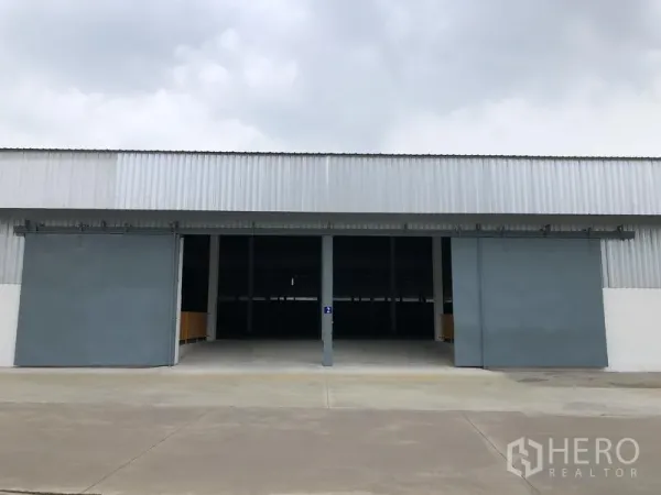 คลังสินค้า ให้เช่าในNonthaburi - มุมมองด้านหน้าของโกดังพร้อมประตูสไลด์เหล็กขนาดใหญ่สองบานและลานคอนกรีตกว้าง