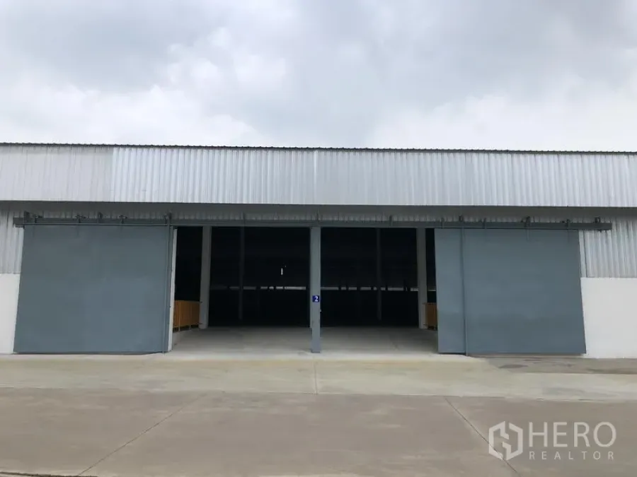 คลังสินค้า ให้เช่าในNonthaburi - มุมมองด้านหน้าของโกดังพร้อมประตูสไลด์เหล็กขนาดใหญ่สองบานและลานคอนกรีตกว้าง